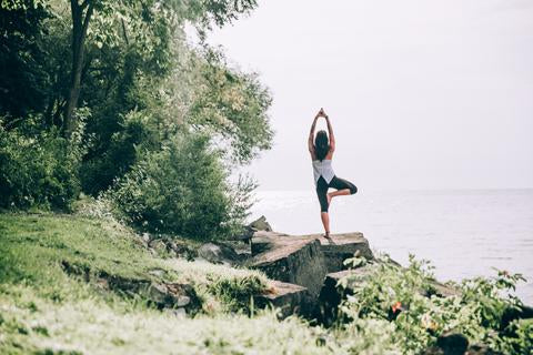 Woman on rock overlooking water in yoga pose